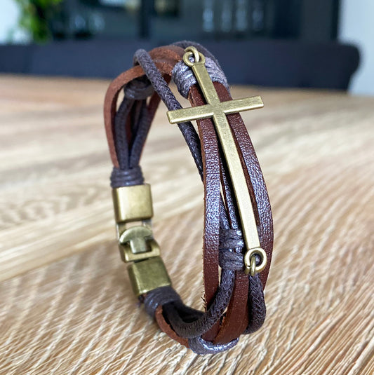 Handmade men's leather bracelet with brass cross and clasp on wooden table – Christian gift for him