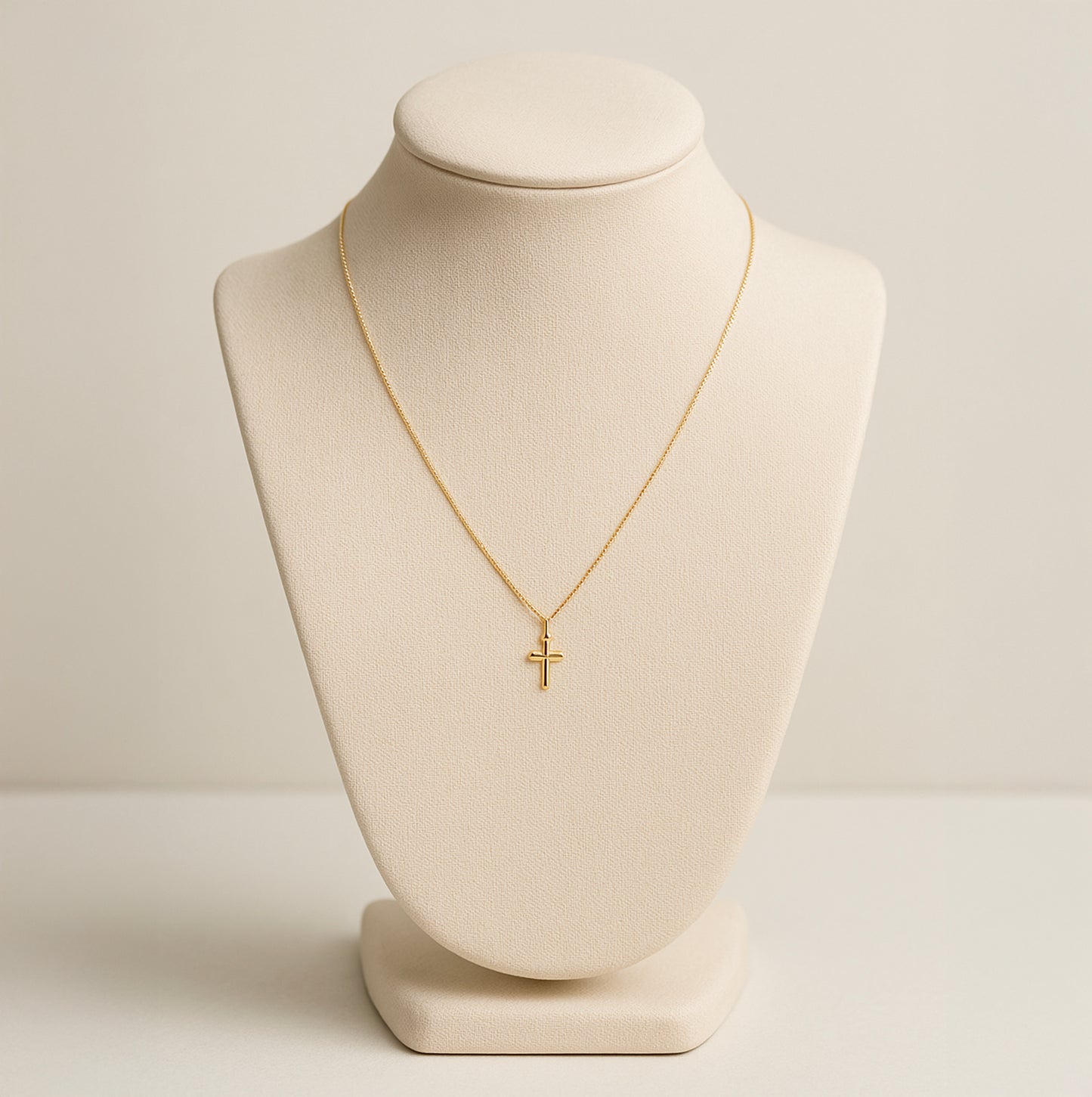 Dainty 18K gold cross necklace on beige display bust with thin chain and small cross pendant
