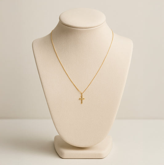 Dainty 18K gold cross necklace on beige display bust with thin chain and small cross pendant