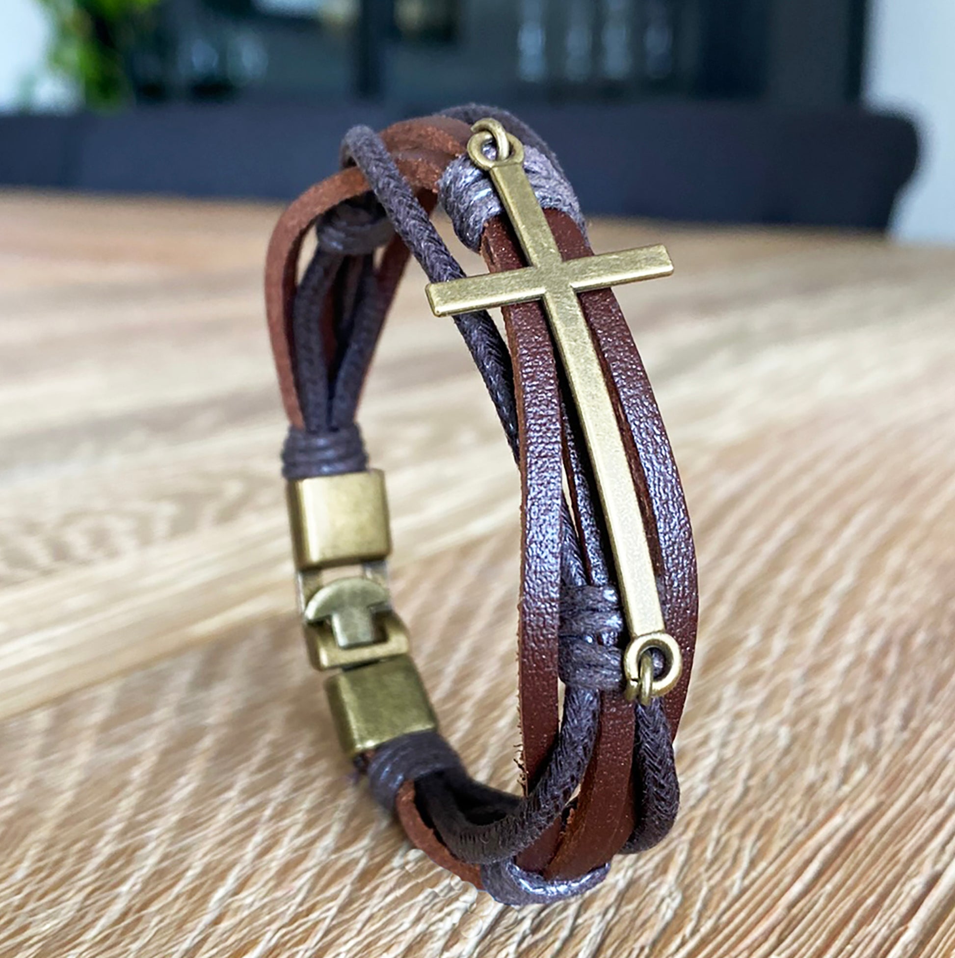 Handmade men's leather bracelet with brass cross and clasp on wooden table – Christian gift for him