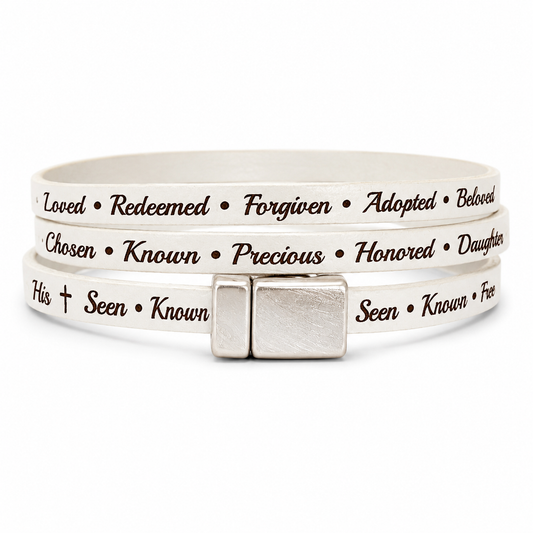 leather wrap-style bracelet with silver-toned rectangular clasp, featuring engraved black text words of affirmation such as 'Loved', 'Redeemed', 'Forgiven', 'Adopted', 'Beloved', 'Chosen', 'Known', 'Precious', 'Honored', 'Daughter', 'His', 'Seen', 'Known', and 'Free'.
