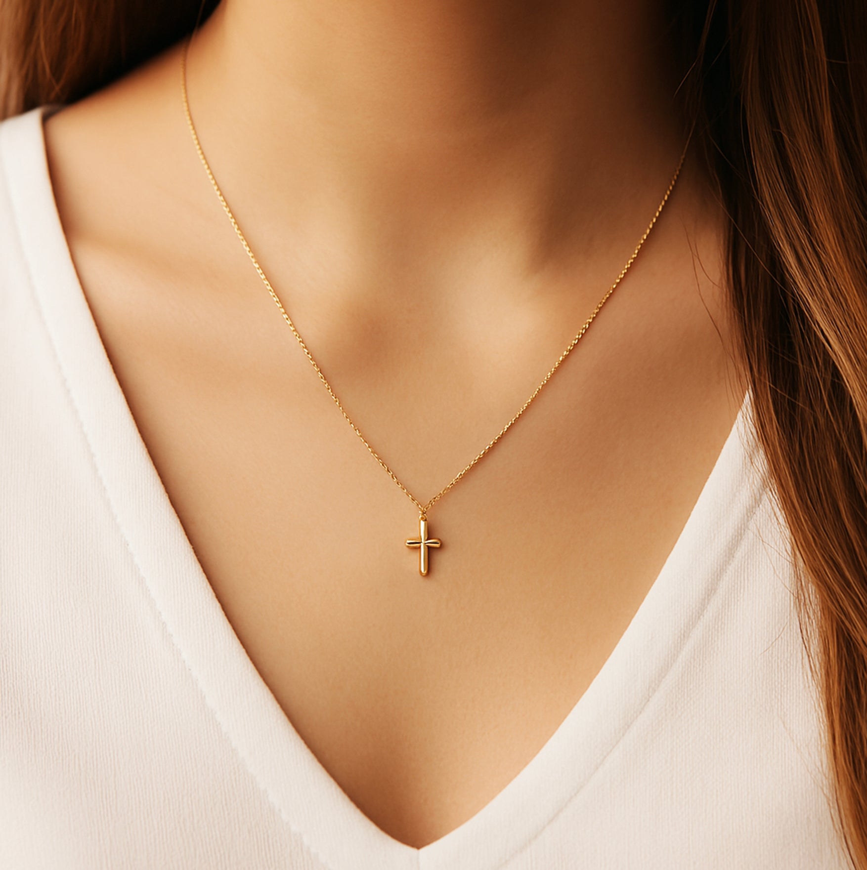 Woman wearing delicate 18K gold cross necklace with minimalist pendant on collarbone.