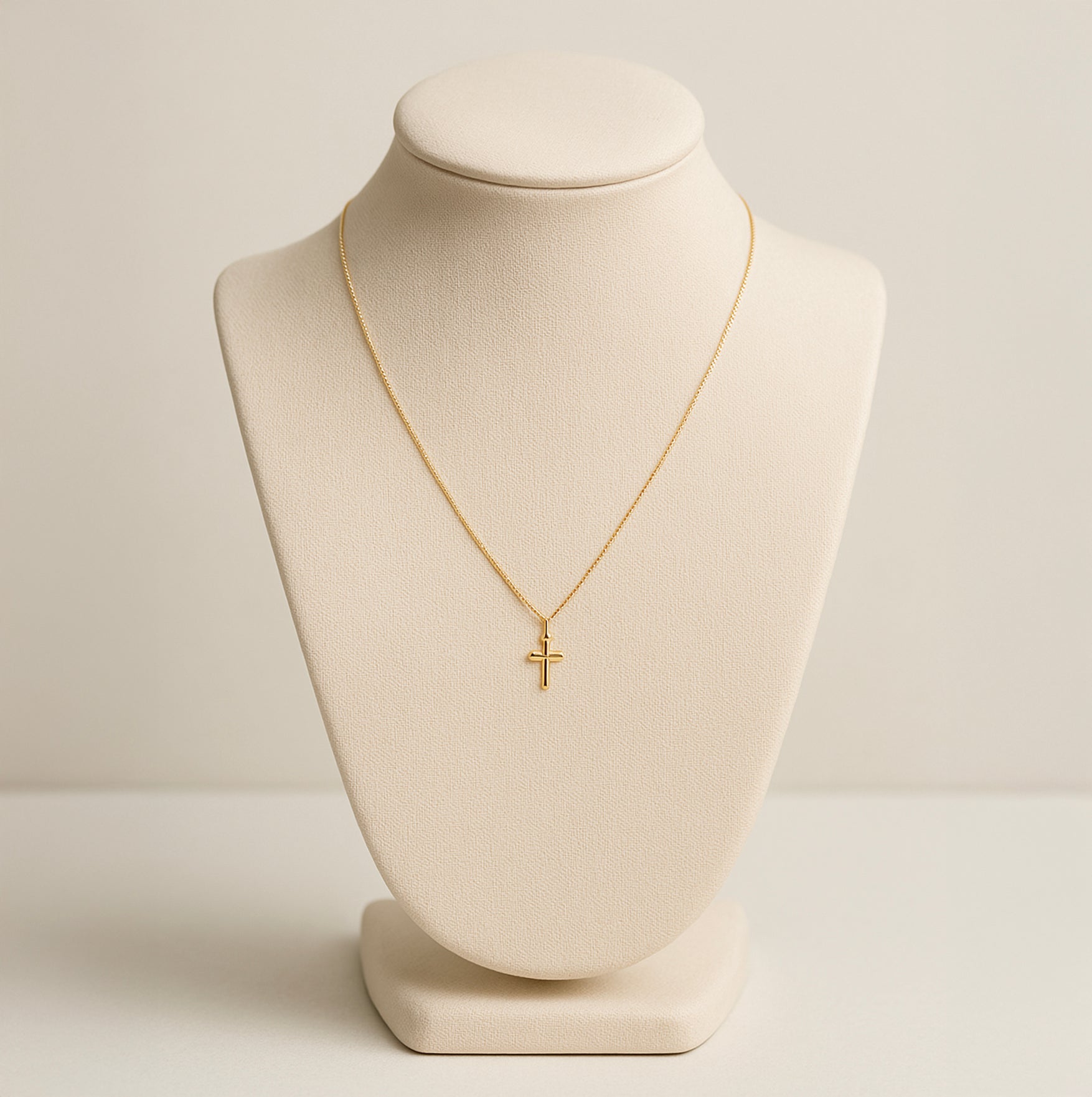 Dainty 18K gold cross necklace on beige display bust with thin chain and small cross pendant